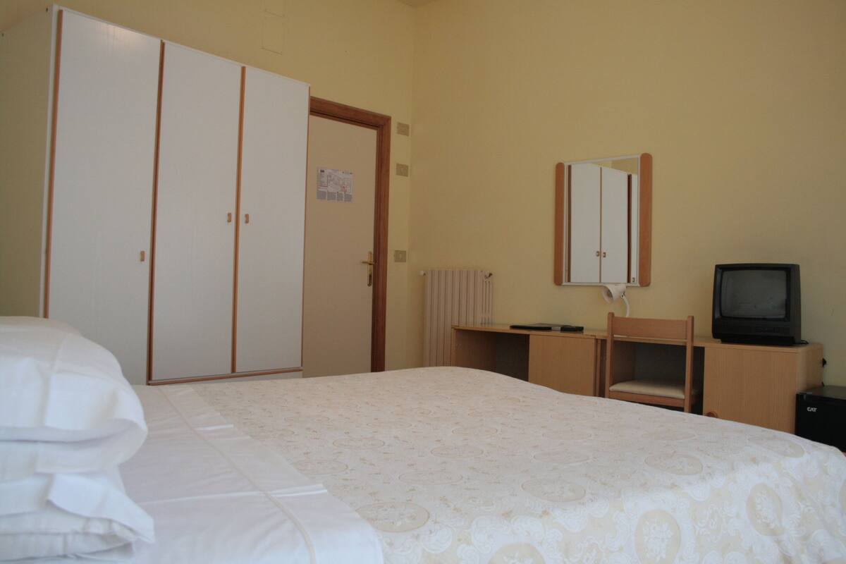 Une chambre d’hôtel comprenant un lit, une armoire, un bureau avec une chaise, une télévision et un radiateur.