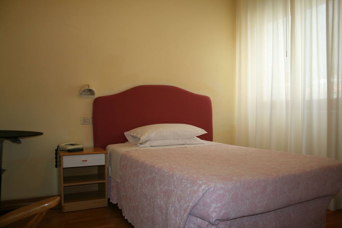 Une chambre à coucher avec un lit simple, une table de chevet, une commode et une fenêtre avec des rideaux.