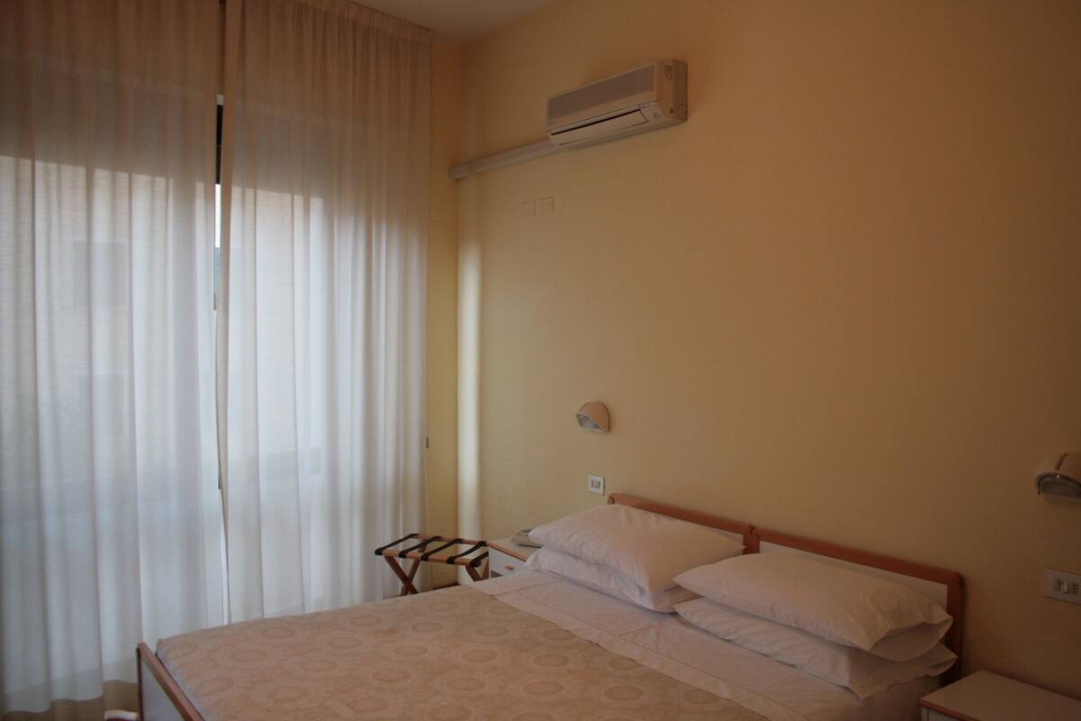 Une chambre d’hôtel avec un lit, un appareil de climatisation, une table de chevet et une fenêtre avec des rideaux.