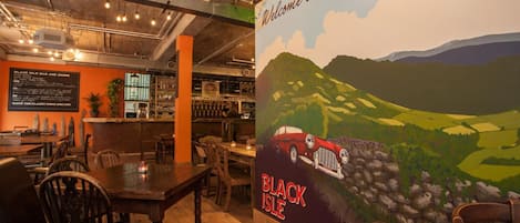 A restaurant interior with a mural of a car on a hill, wooden tables, and chairs.