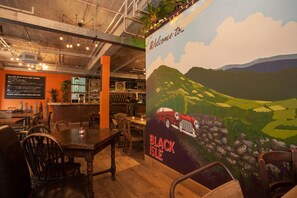 A restaurant interior with a mural of a car on a hill, wooden tables, and chairs.
