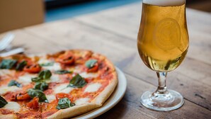 A pizza with basil and tomato slices on a plate next to a glass of beer on a wooden table. - Black Isle Bar and Rooms (Inverness)
