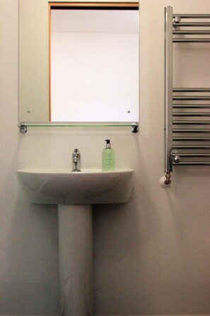 A bathroom with a white sink, a glass shelf above it, and a towel rack to the right.