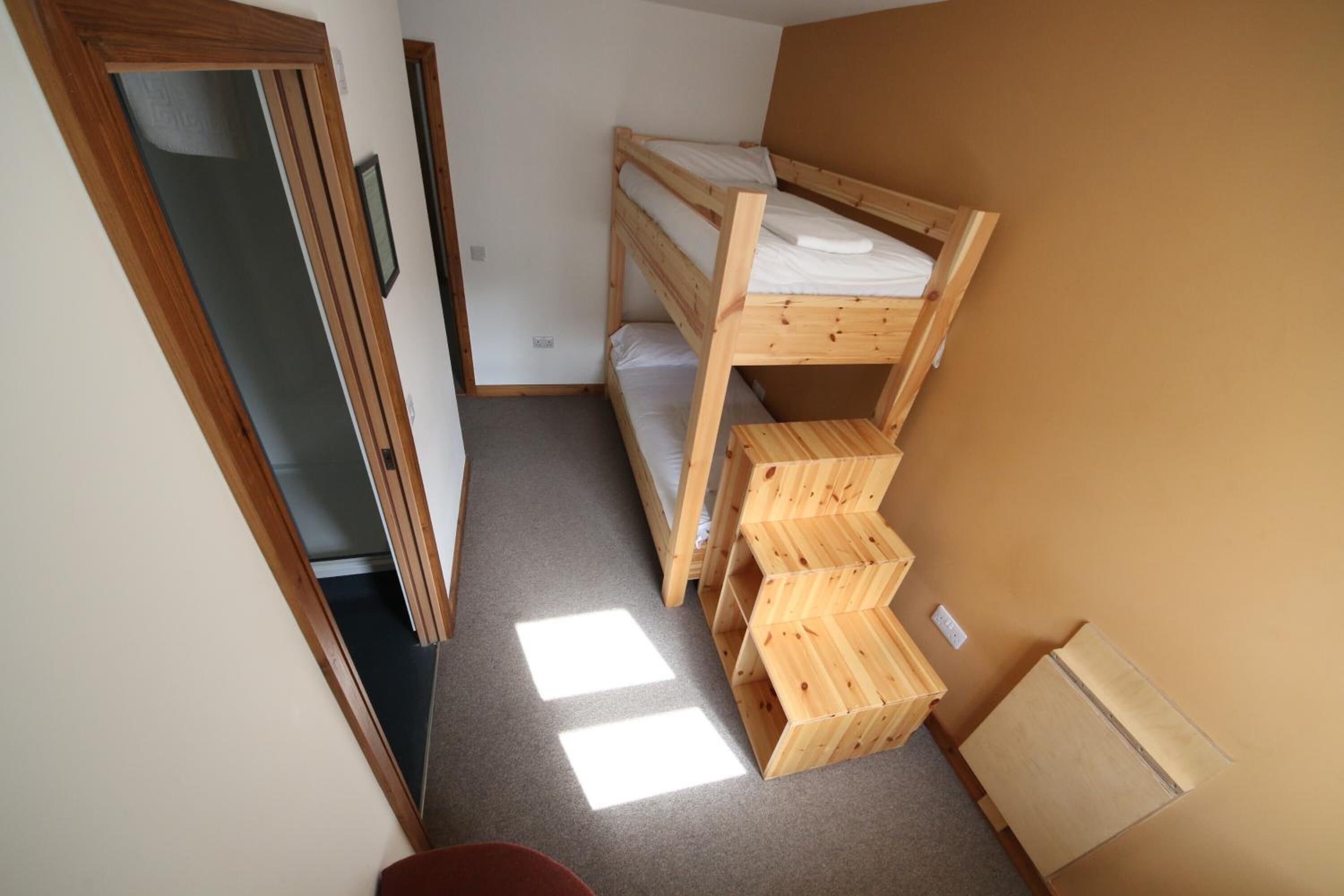 Een kleine, praktische kamer met een stapelbed, een houten wandplank en een radiator.