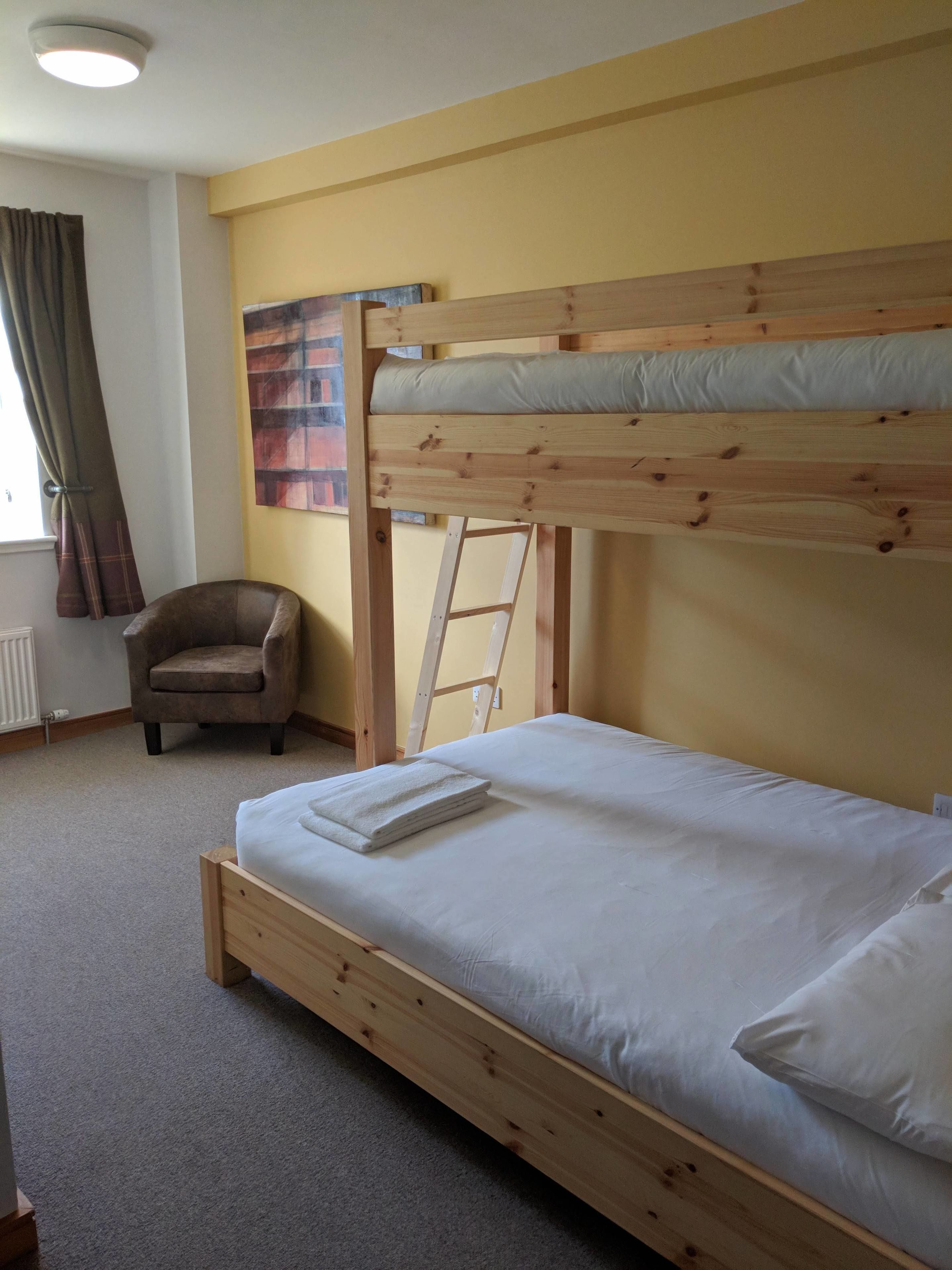 Una cama litera con una escalera, una silla y un radiador en una habitación con paredes amarillas.