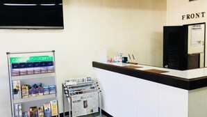 A reception desk with a 'FRONT' sign, a television mounted above, and a magazine rack with various publications. - Green Hotel Shimonoseki (Shimonoseki)
