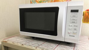 Un microondas blanco con pantalla digital y botones de control sobre una mesa con mantel estampado.
