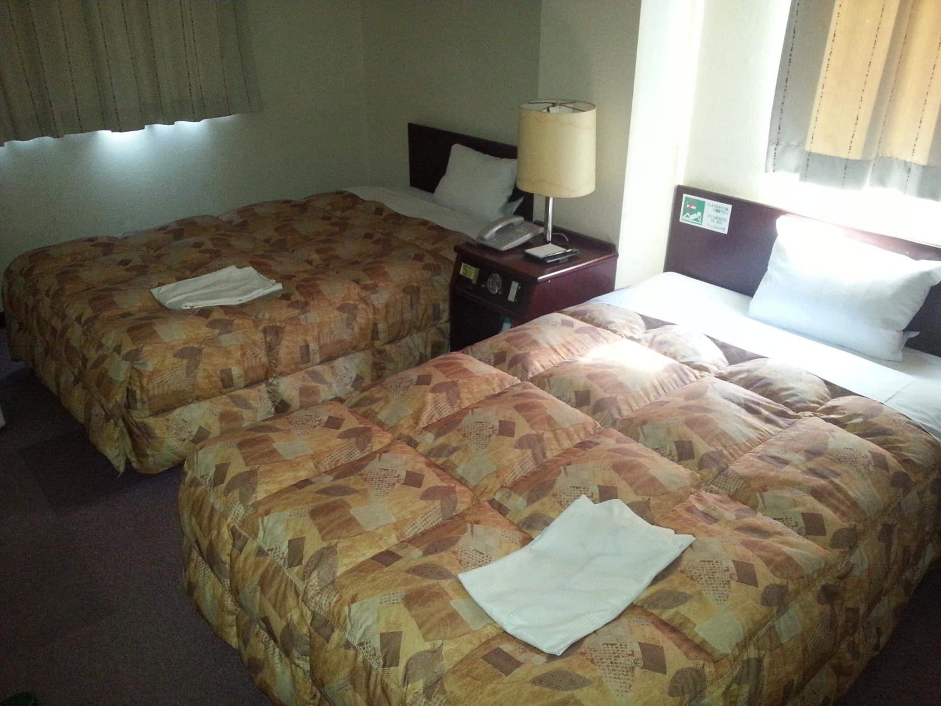 Habitación de hotel con dos camas, una mesita de noche con lámpara y una ventana con cortinas.