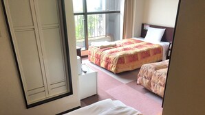 Habitación de hotel con dos camas, un escritorio pequeño blanco y una ventana con vistas a la vegetación.