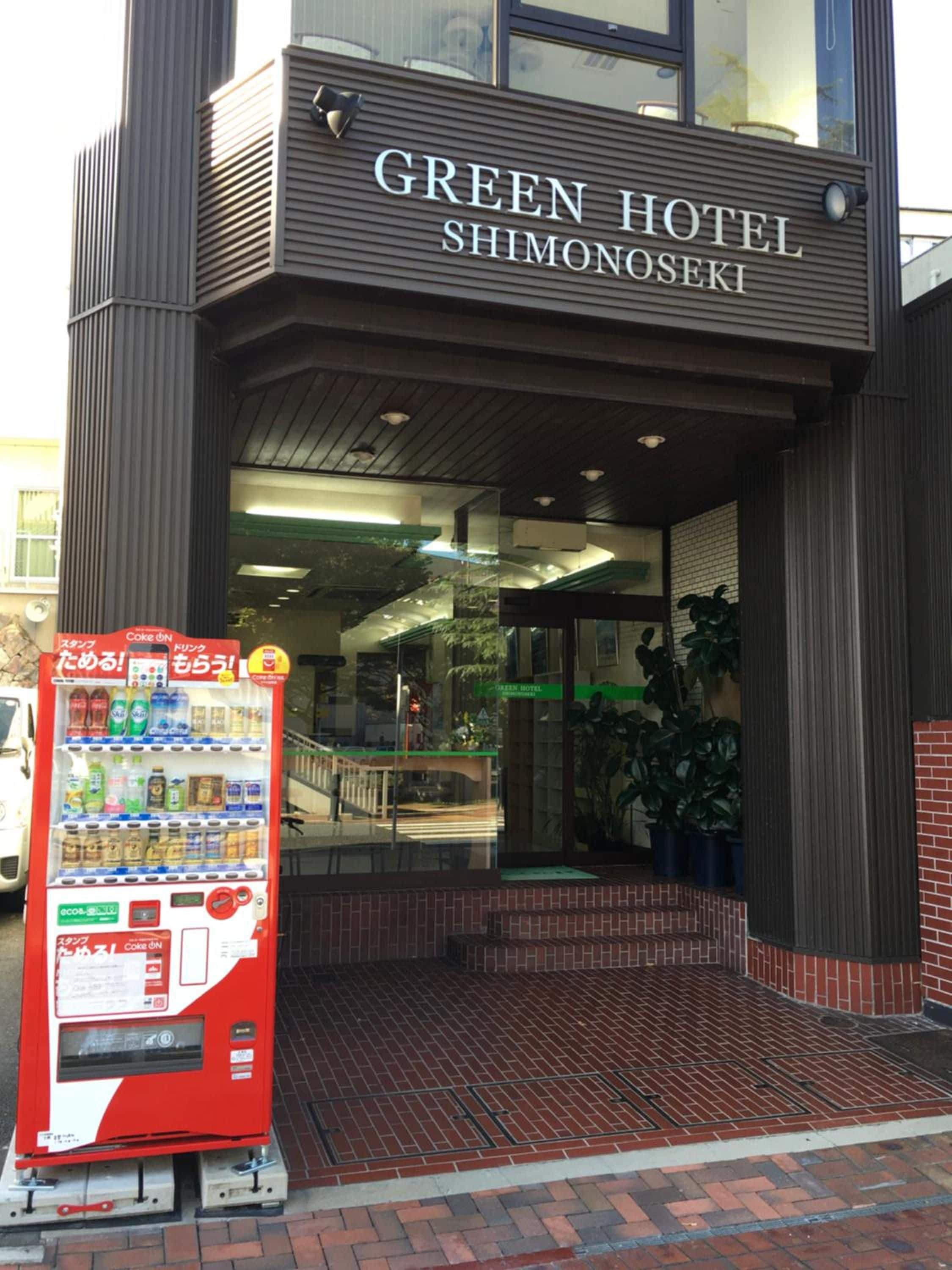 The exterior of the Green Hotel Shimonoseki with a vending machine in front.