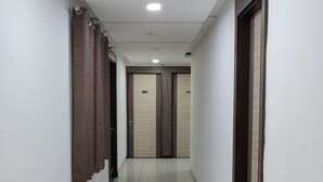 A clean, well-lit hallway with tiled floors, wooden doors, and a ceiling light.