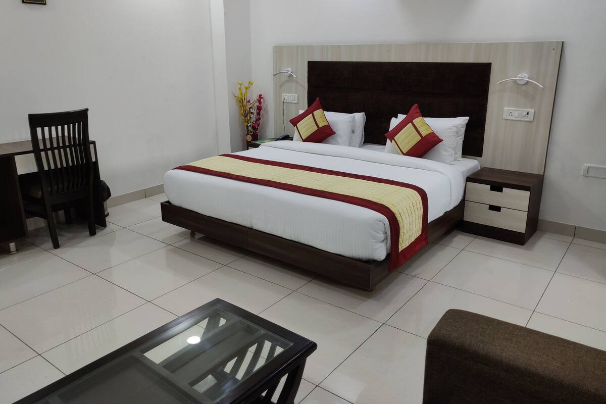 A neatly arranged hotel room with a large bed, a small table, a chair, and a nightstand.