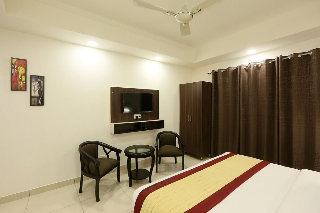 Habitación de hotel con cama, televisión montada en la pared, dos sillas, una mesita y un armario.