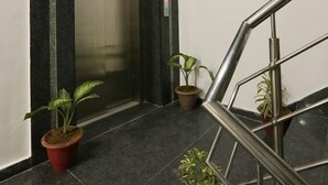 An elevator with a marble wall, a green emergency exit sign, and potted plants.