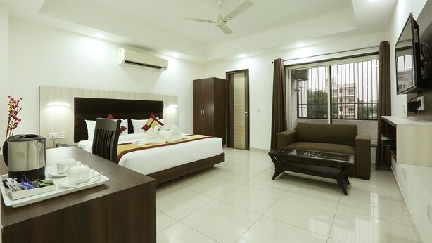 A hotel room with a bed, a sofa, a coffee table, a desk with a tray of breakfast items, a TV, and a large window with blinds.