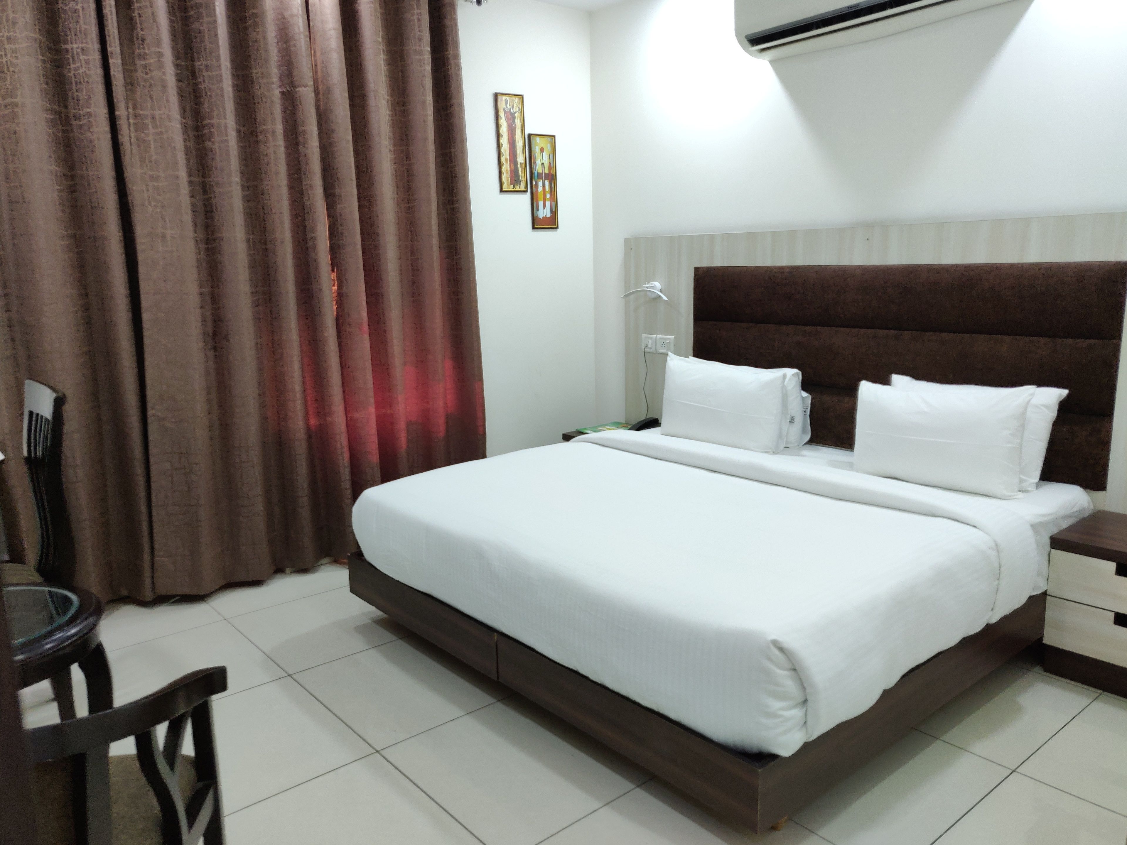 A hotel room with a large bed, a bedside table, a chair, and a curtain.