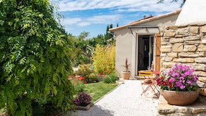 A house with a stone exterior, a gravel pathway, and a garden with various plants and flowers. - Gite Les Aiguillans (Mérindol-les-Oliviers)