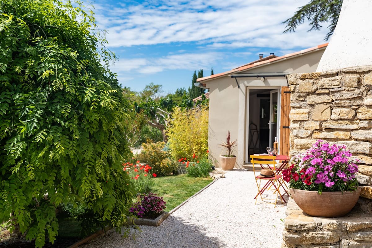 Una casa amb façana de pedra, un camí de grava i un jardí amb plantes i flors variades.