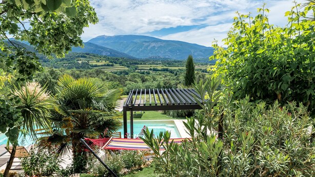 A pool area with a pergola, surrounded by lush greenery and a mountainous landscape in the background. - Gite Les Aiguillans (Mérindol-les-Oliviers)