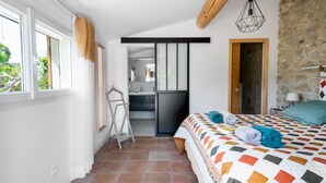 A bedroom with a bed, a window, a door, and a view of a kitchen and bathroom. - Gite Les Aiguillans (Mérindol-les-Oliviers)