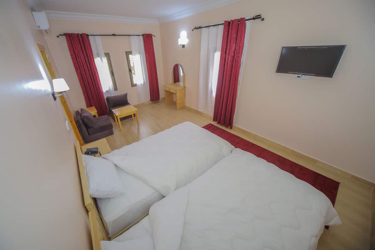 Quarto de hotel com uma cama grande, uma escrivaninha, uma cadeira, um espelho e uma televisão.