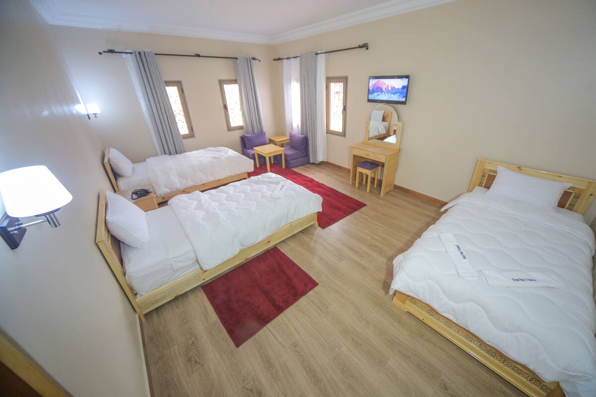 Quarto de hotel com duas camas, uma televisão, uma escrivaninha e uma cadeira.