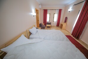 A hotel room with a large bed, a small table, a chair, a desk, and a mirror. - Ksar Ben Youssef (Tarmigt)