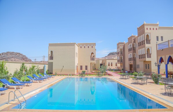 A swimming pool with lounge chairs and a building with arched windows and balconies. - Ksar Ben Youssef (Tarmigt)