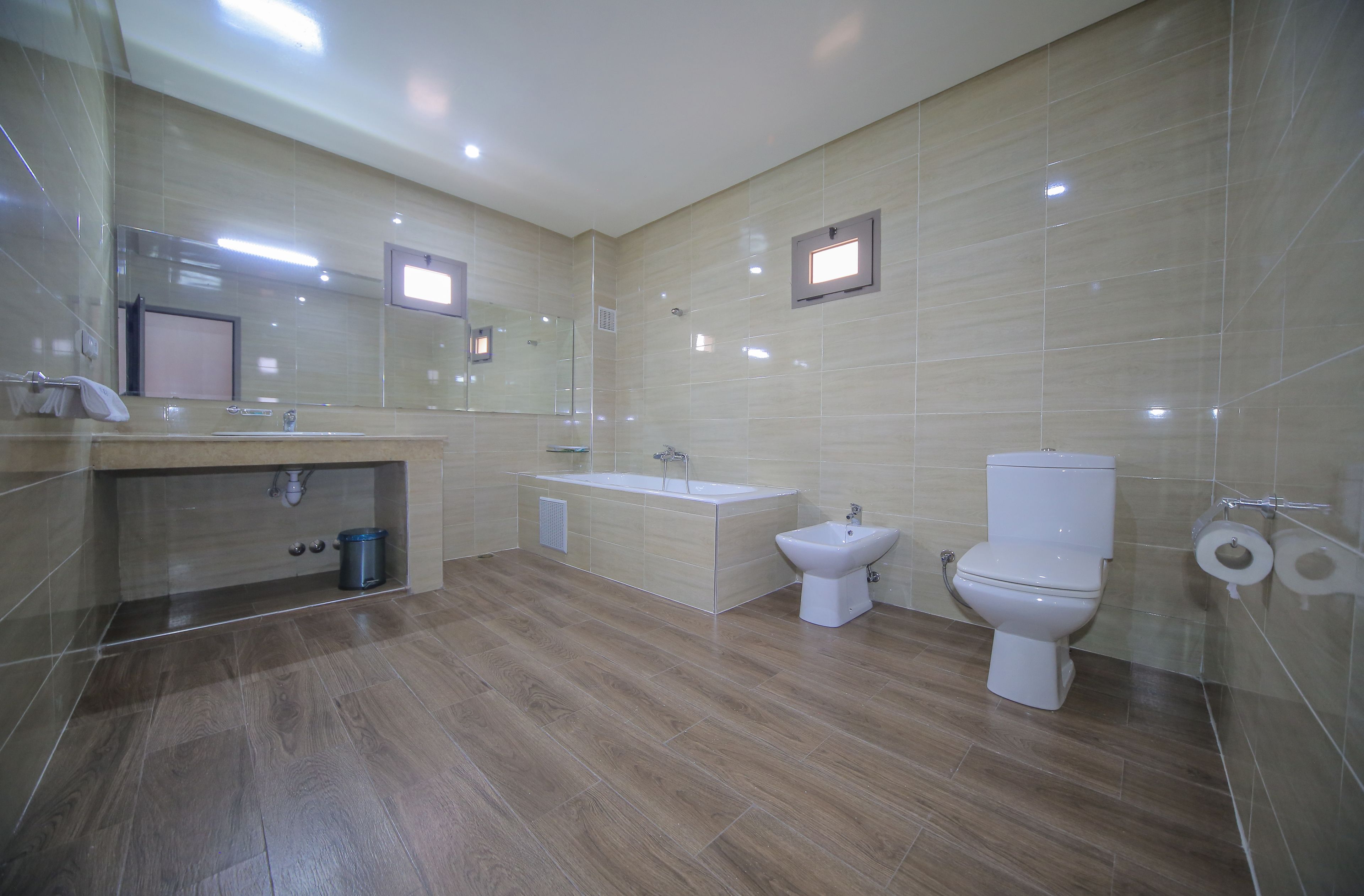 Een moderne badkamer met een houten vloer, een wastafel, een badkuip, een toilet en een douchetoilet.
