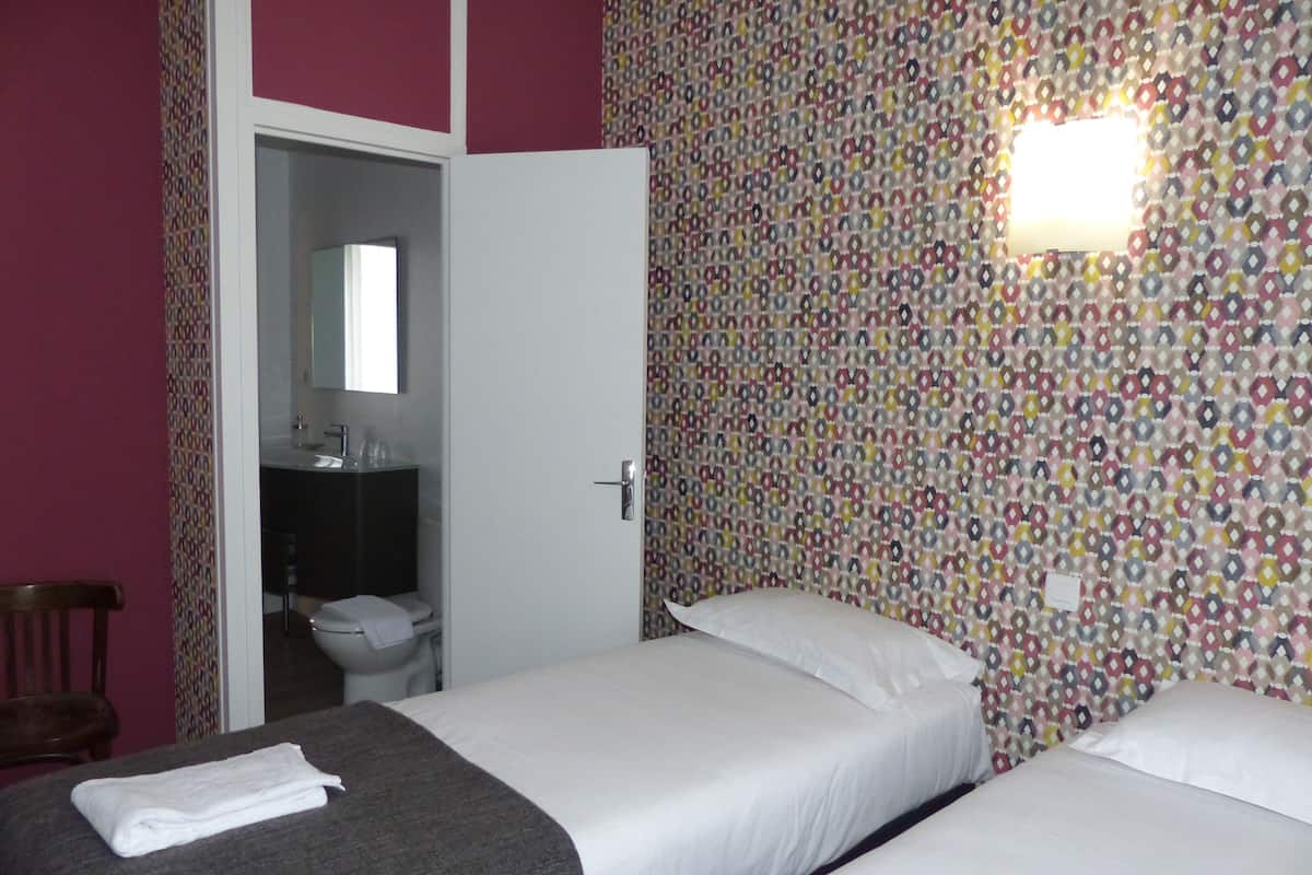 A hotel room with two beds, a bathroom, and a patterned wall.