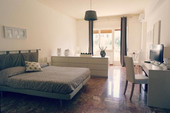 A bedroom with a bed, a desk, a chair, a television, and a window with curtains.