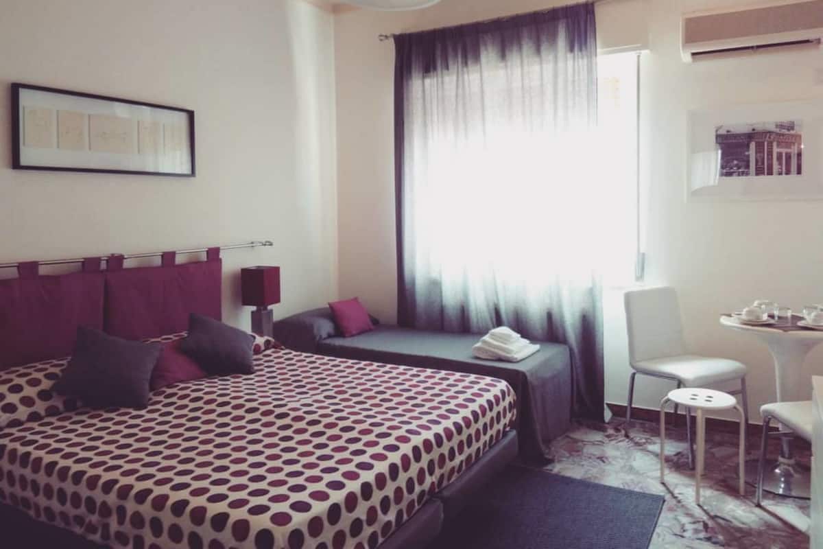 A hotel room with a large bed, a smaller bed, a desk with a chair, and a window with curtains.