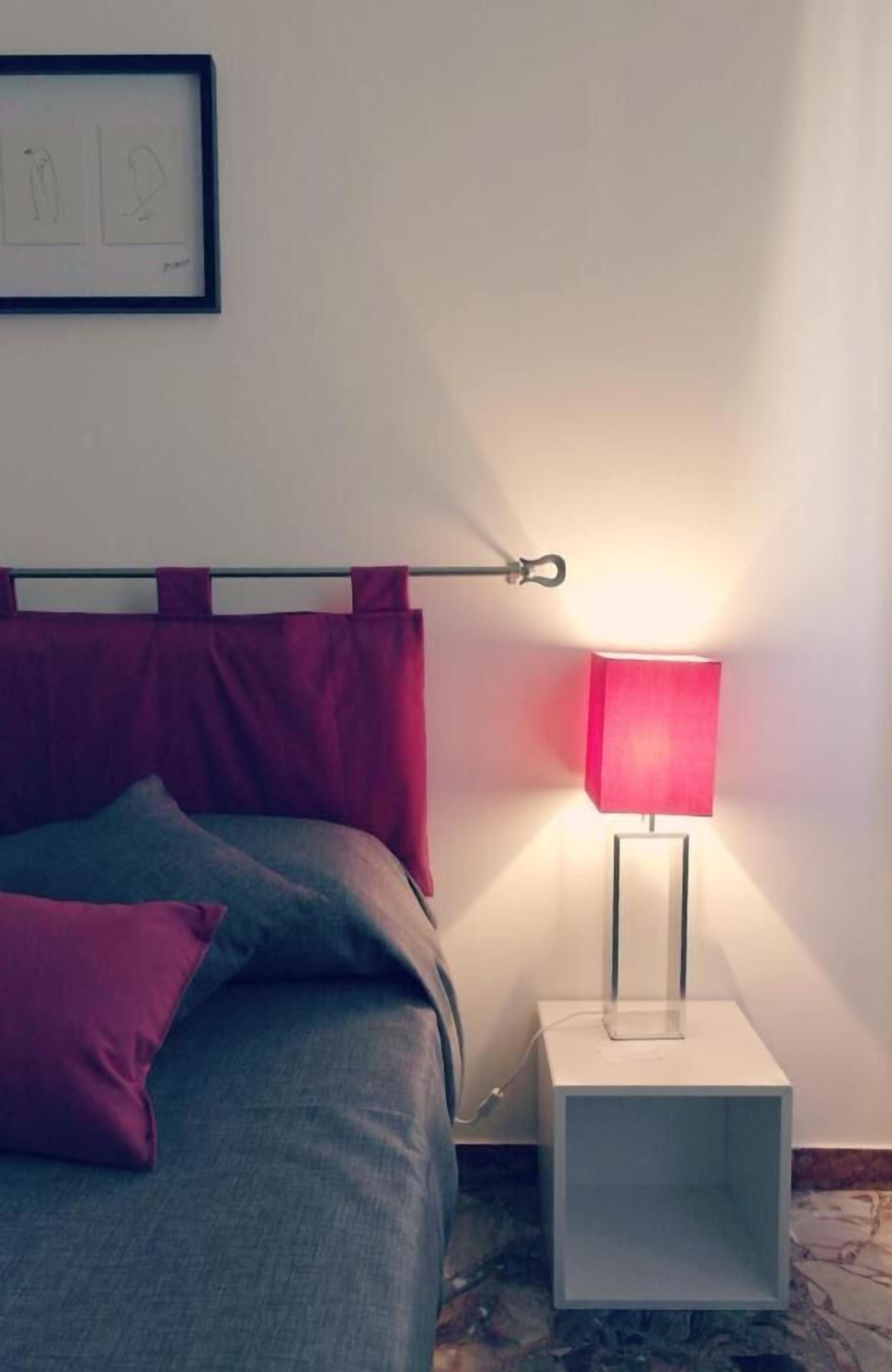 Uma cama bem arrumada com cabeceira, uma mesa de cabeceira com abajur e um quadro na parede.