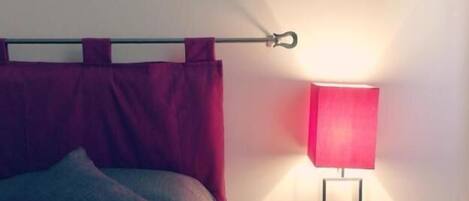 Uma cama bem arrumada com cabeceira, uma mesa de cabeceira com abajur e um quadro na parede.