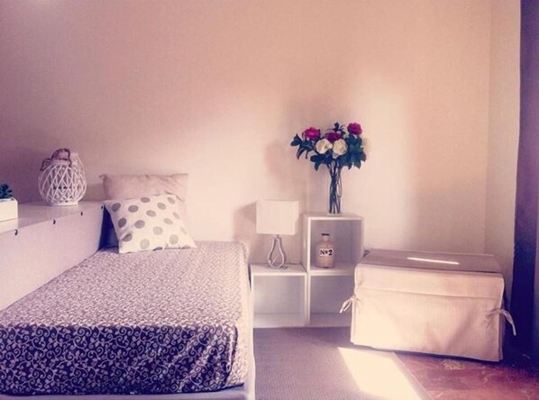 A bedroom with a bed, a nightstand, a lamp, a vase with flowers, and a chest of drawers. - B&B La Peonia (Reggio Calabria)