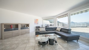 A modern living room with a sectional sofa, glass coffee table, and a view of the beach. - Centro Cadro Panoramica (Lugano)