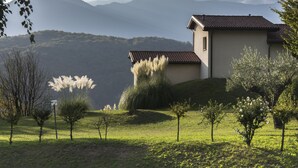 A house with a sloped roof, surrounded by a grassy landscape and trees, with mountains in the background. - Centro Cadro Panoramica (Lugano)