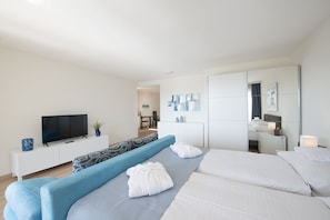 Habitación de hotel moderna con una cama grande, televisión, sofá y un área de comedor a la vista.