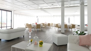 A spacious, modern living area with a white sofa, a coffee table with decorative items, and a dining area with round tables and chairs. - Centro Cadro Panoramica (Lugano)