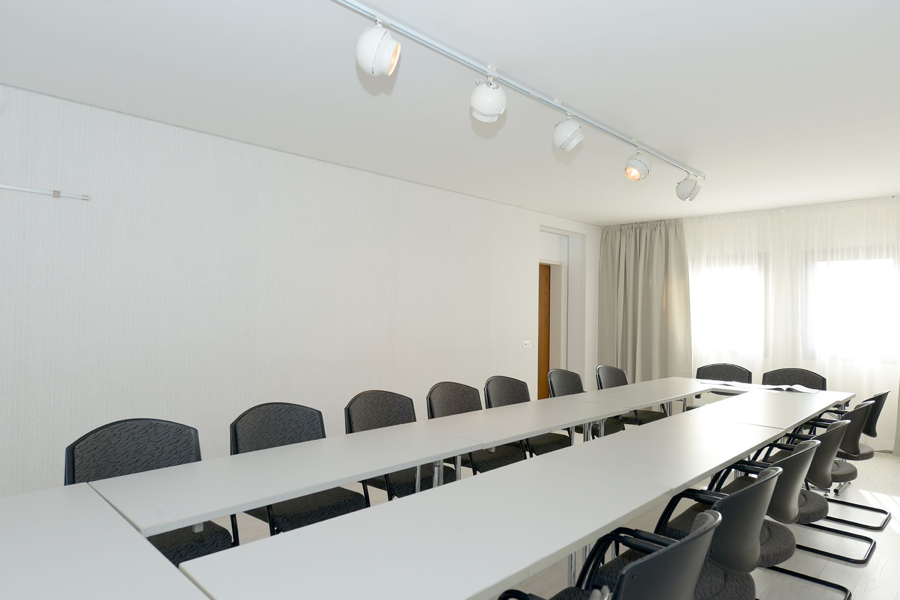 A conference room with a long table and chairs, white walls, and ceiling lights.