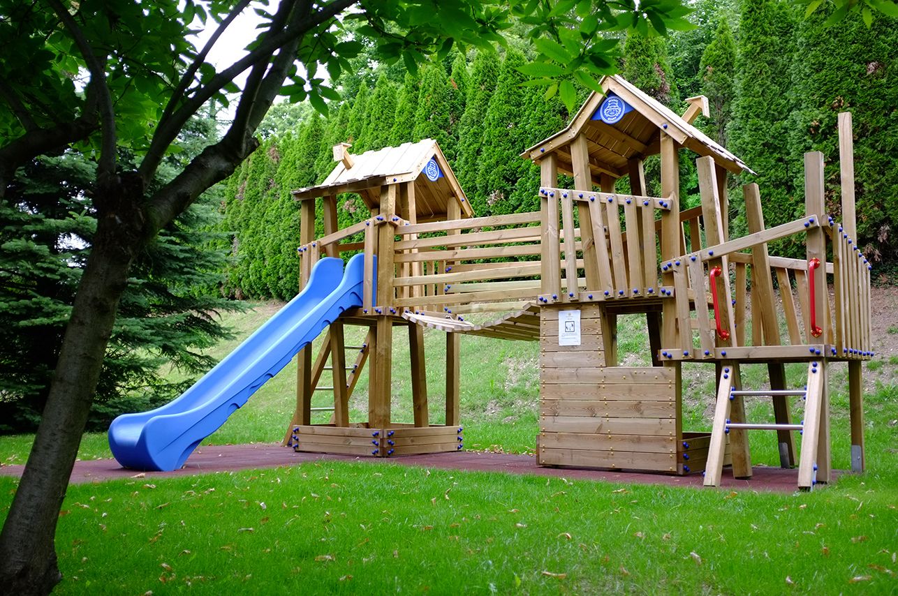 A wooden playground structure with a blue slide and climbing elements.