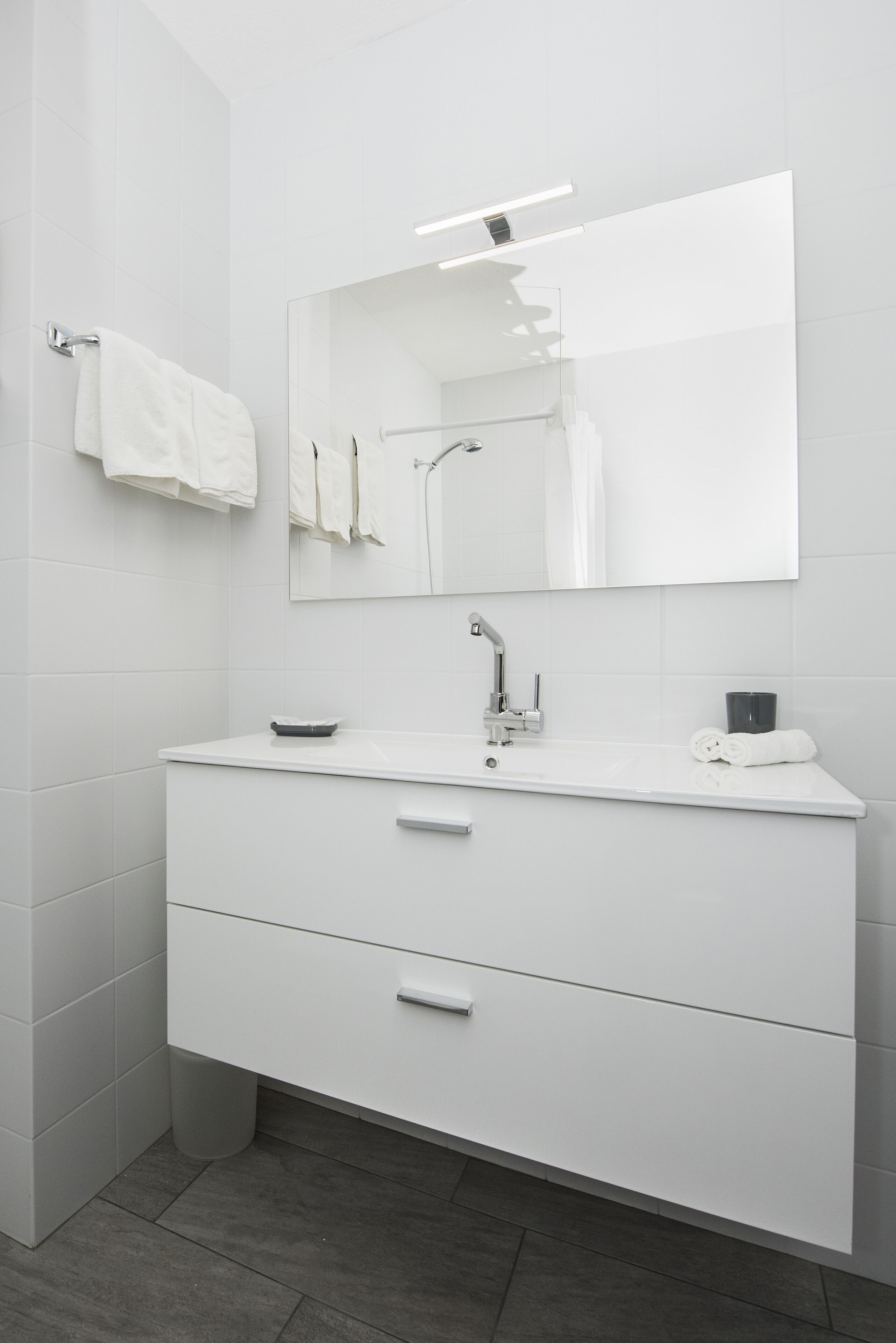 A modern bathroom with a white vanity, a mirror, and a towel rack.