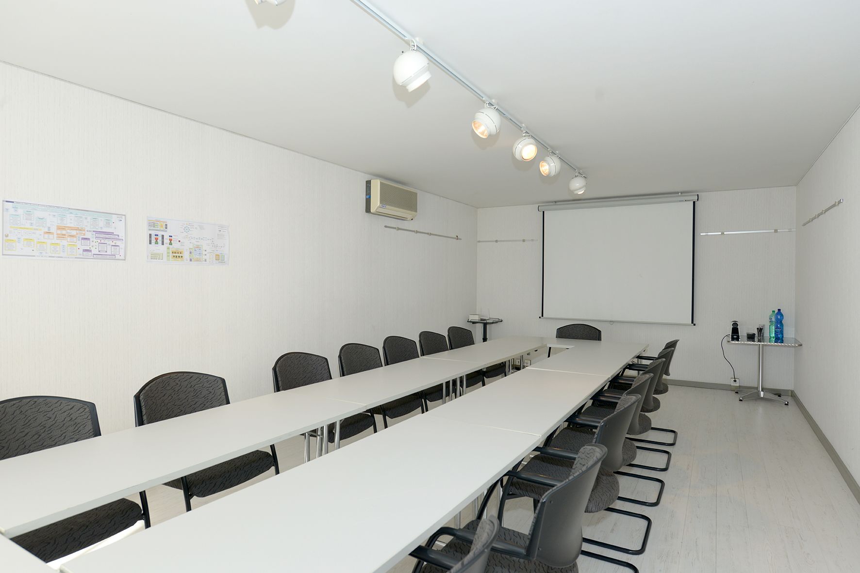 Ein Konferenzraum mit einem langen Tisch, Stühlen, einer Projektionsleinwand und einer Whiteboard-Tafel.