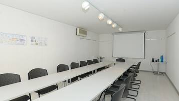 Ein Konferenzraum mit einem langen Tisch, Stühlen, einer Projektionsleinwand und einer Whiteboard-Tafel.