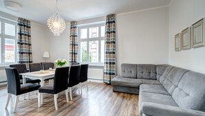 Un salon moderne avec un canapé d’angle gris, une table à manger avec des chaises et un lustre.