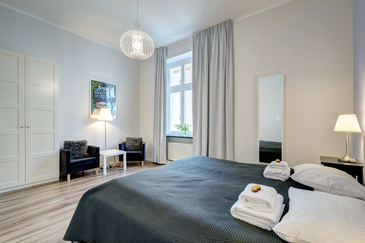 Une chambre d’hôtel avec un grand lit, un bureau, une chaise, un luminaire suspendu et une fenêtre avec des rideaux.