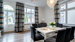 Un espace repas avec une table blanche, des chaises à revêtement noir et un lustre.