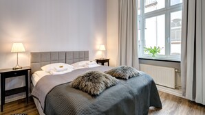 Une chambre à coucher bien rangée, avec un grand lit, deux tables de chevet avec des lampes, une fenêtre avec des rideaux et un radiateur.