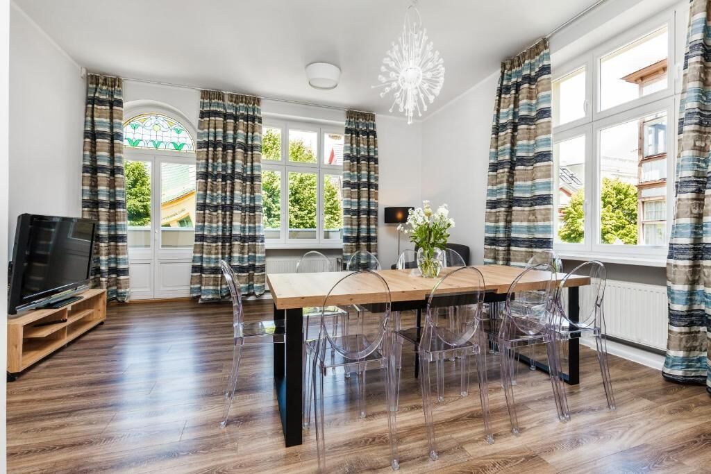 A dining area with a wooden table and clear chairs, a television on a wooden stand, and curtains with a striped pattern.