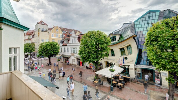 Une place animée, bordée de bâtiments historiques, avec des terrasses de café et un immeuble moderne aux façades vitrées.